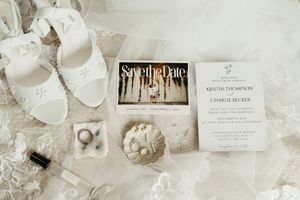 Elegant wedding invitation suite in neutral tones with floral details and delicate paper elements laid out on white surface.