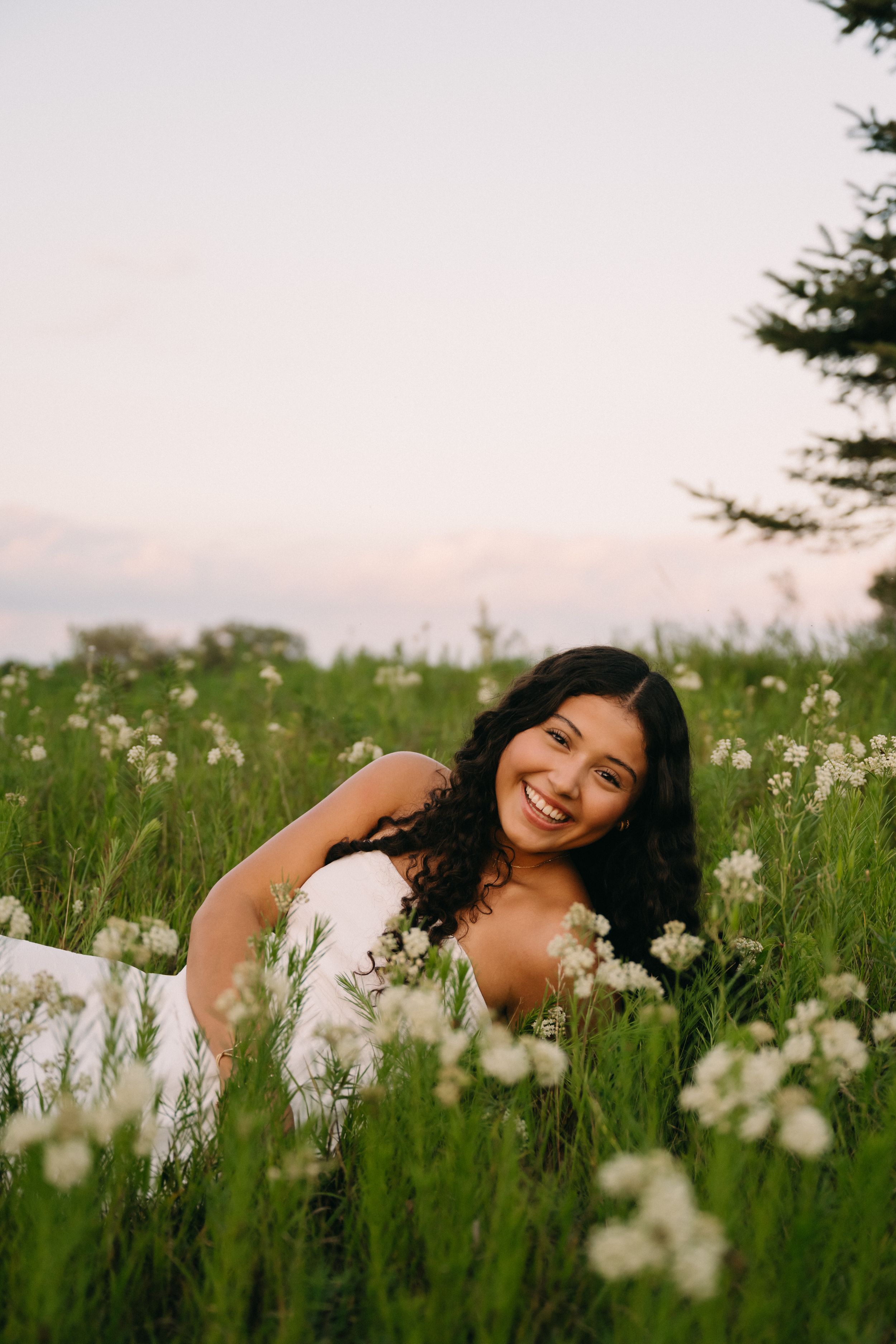 A person lies in a lush green meadow filled with delicate white wildflowers on a summer evening.