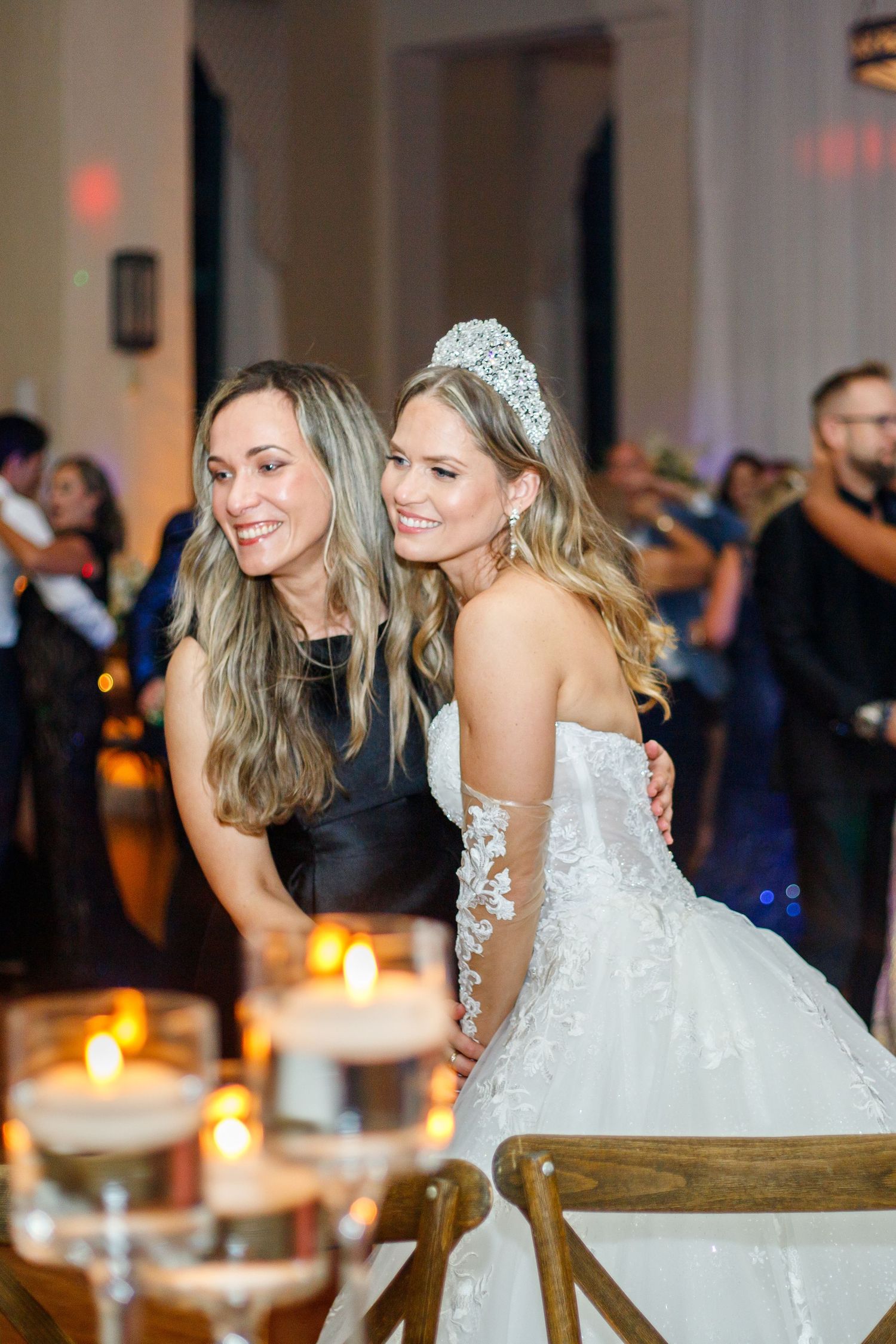 Wedding guests laugh and dance together during reception celebration with candlelit tables and festive atmosphere.