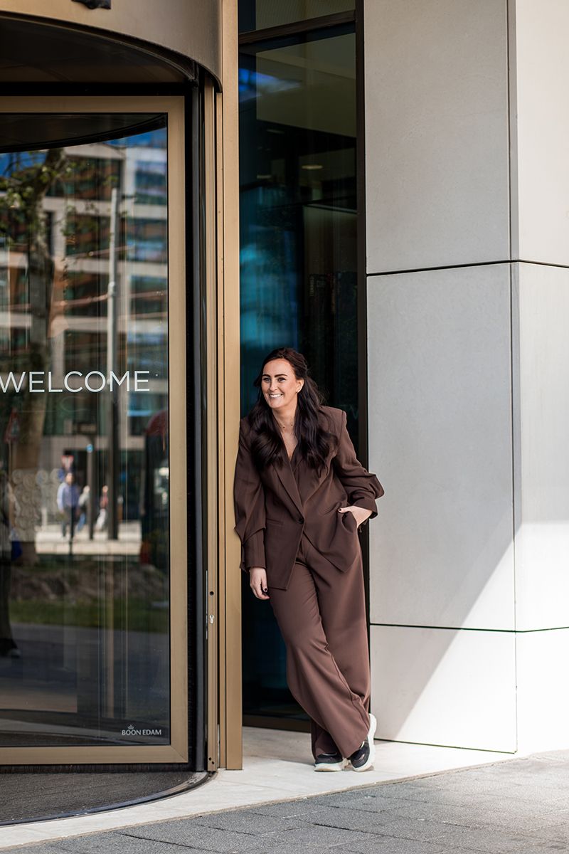 Een personal branding shoot in Amsterdam Zuidas. Een vrouwelijke ondernemer staat lachend bij een gouden draaideur voor een luxe gevoel.
