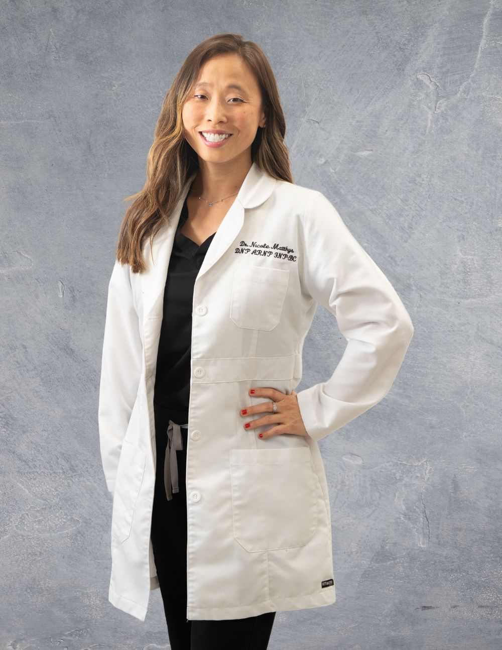 Healthcare professional in white coat and black shirt poses against gray background. Quad Cities Business Headshot Photography