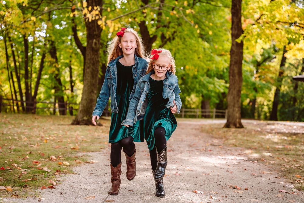 Siblings run playfully on a tree-lined path during fall season.
