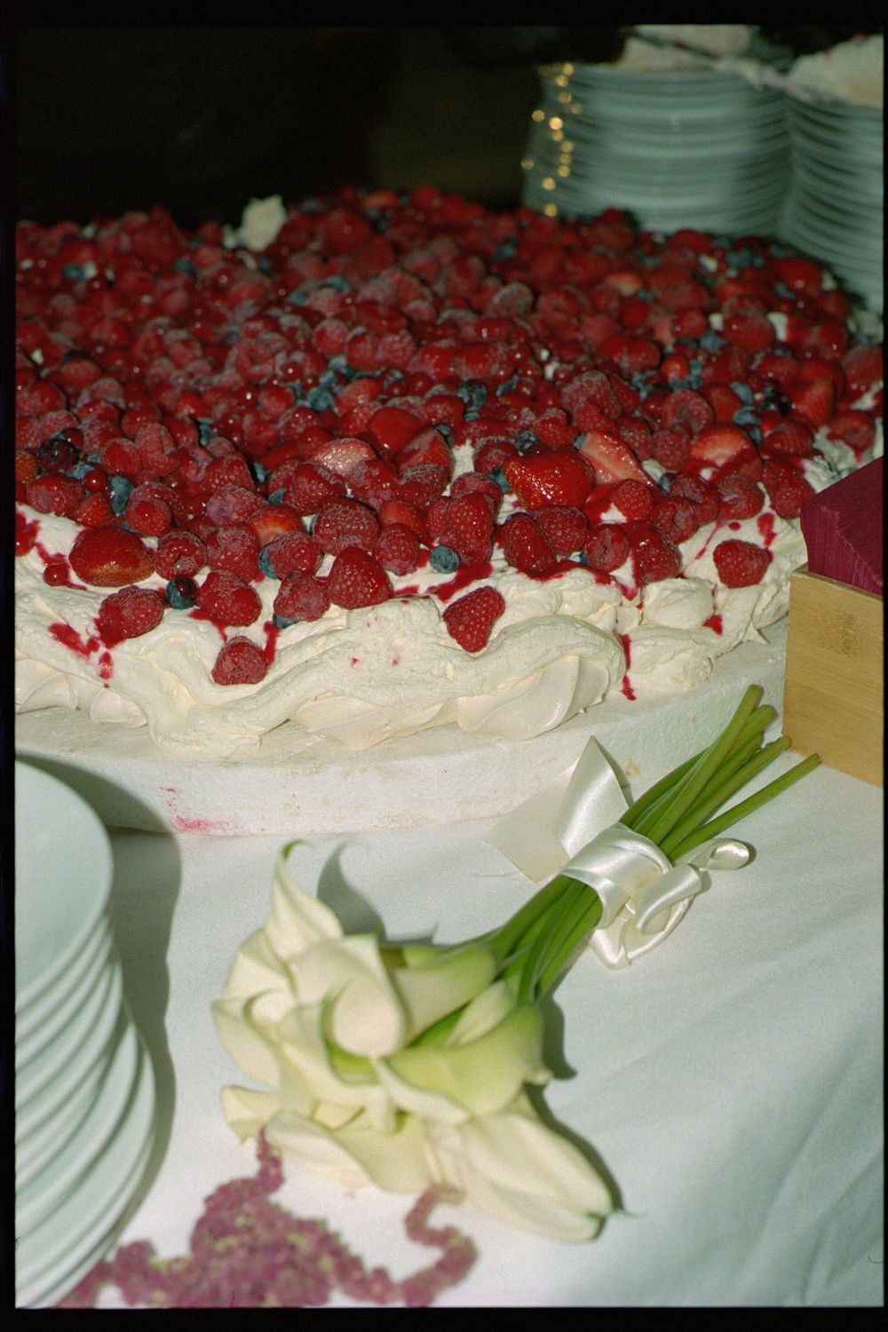 A white frosted cake topped with fresh red raspberries and a white calla lily flower decoration on a table.