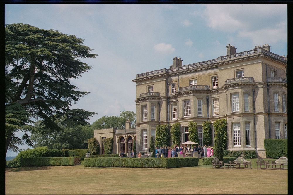Exterior view of a stately English manor house with landscaped grounds and classic architectural features.