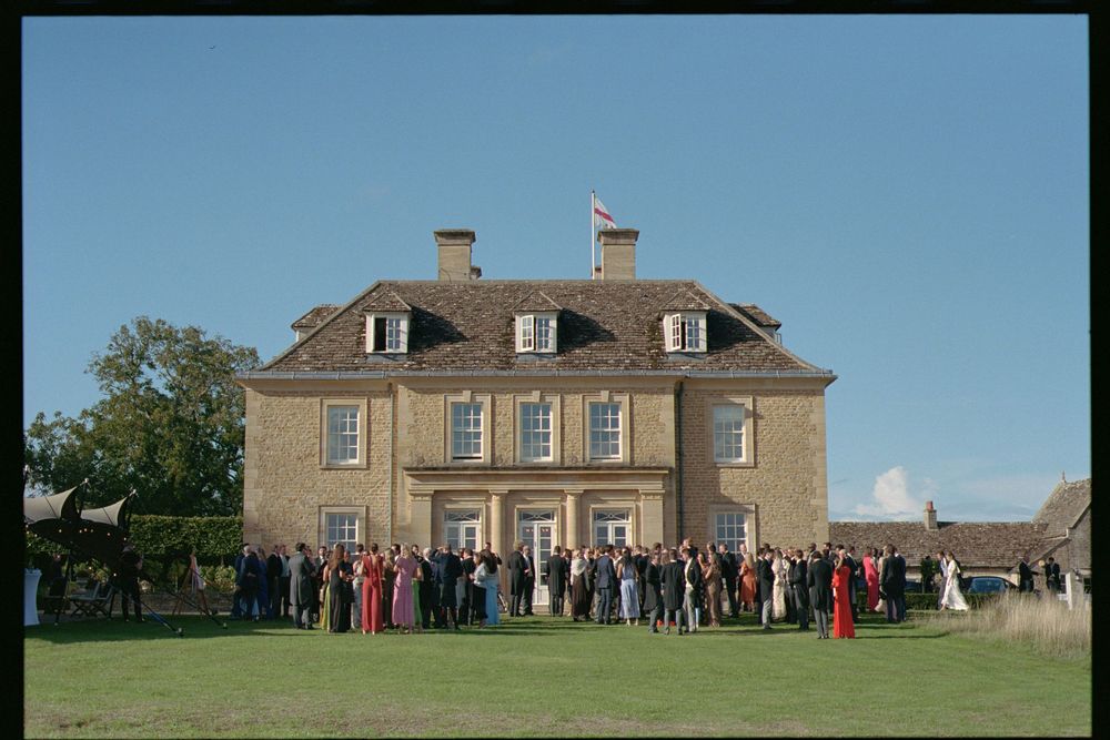 A panoramic view of a historic Georgian mansion with multiple buildings and people gathered on the grounds.