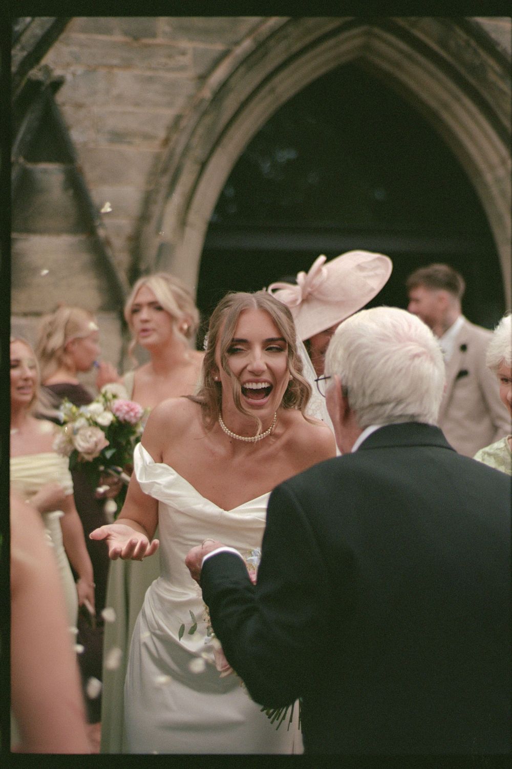 A joyful wedding moment captured outside a church with the bride laughing surrounded by guests.