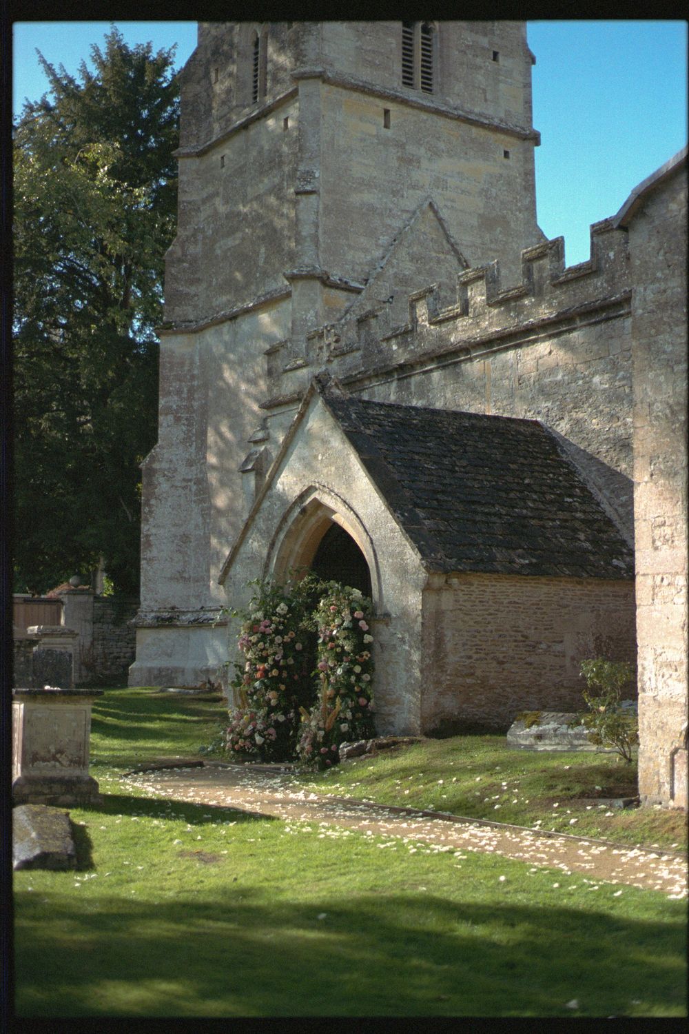 Historic stone church exterior with arched entrance and grassy churchyard surrounded by stone walls in sunlight.