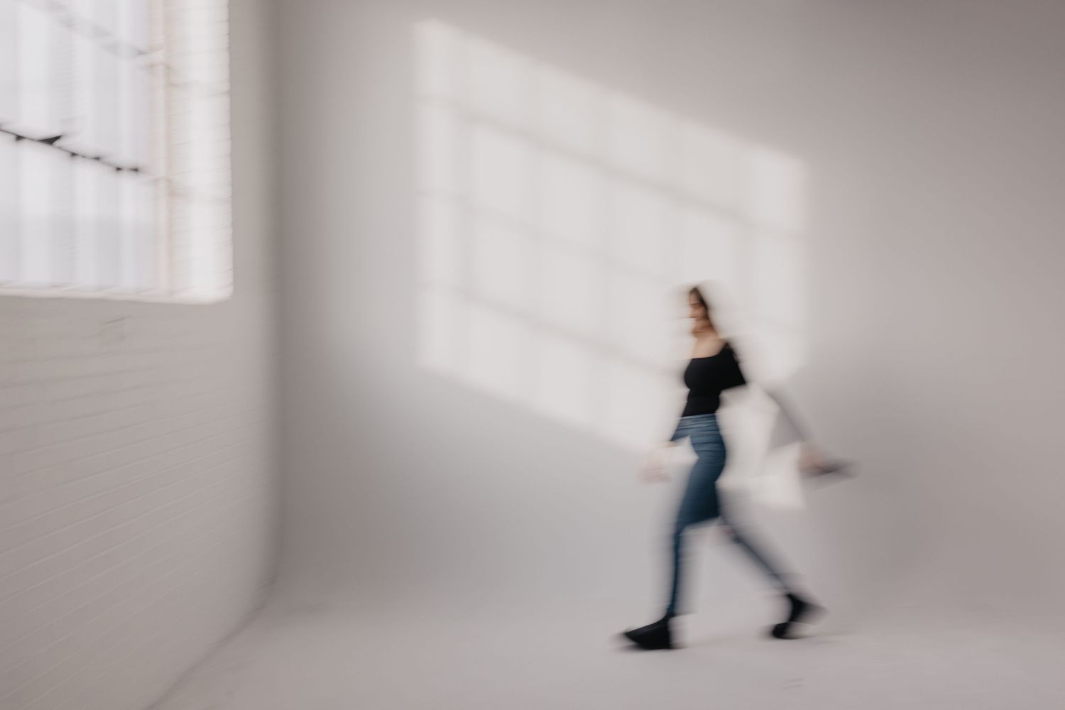 Blurred motion shot of a person walking in a bright white minimalist room.