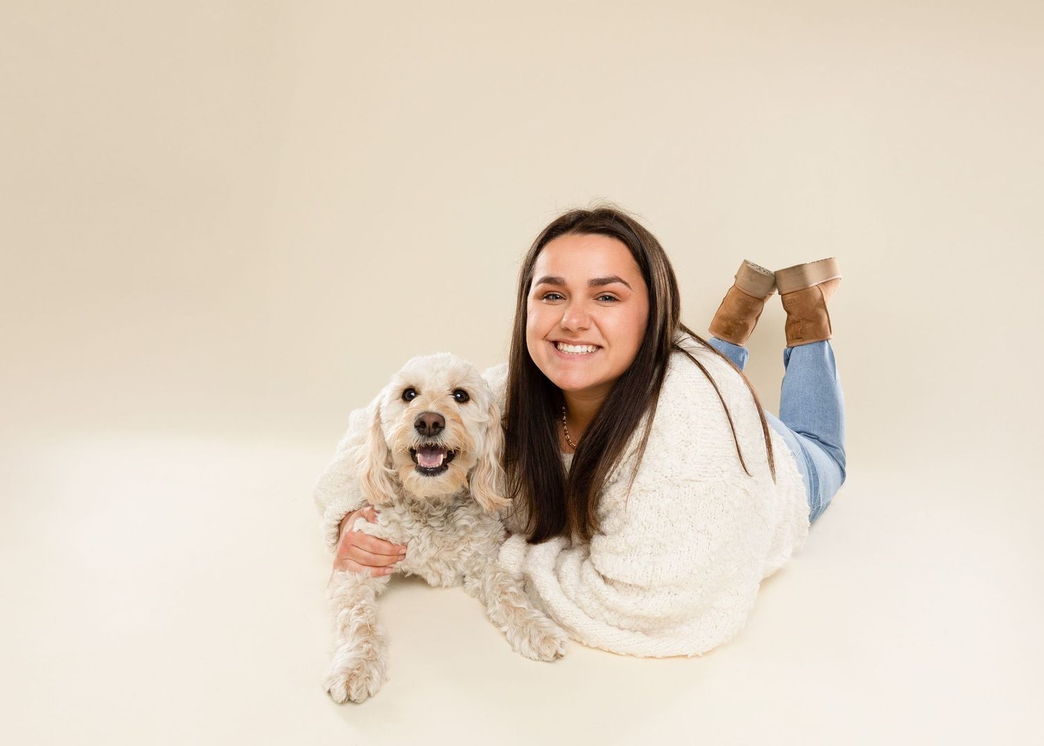 White scruffy dog lounging and playing on cream colored studio background.