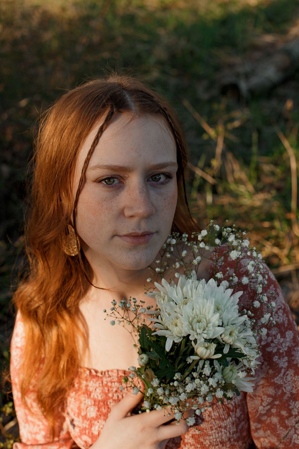 Portrait in a dress holding white chrysanthemums and baby's breath flowers in warm sunset lighting.