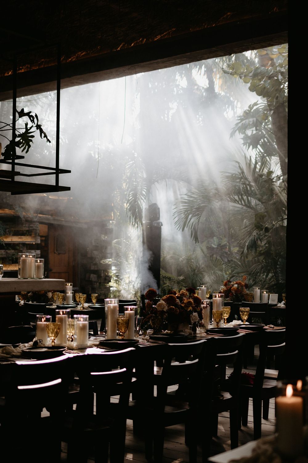 Dramatic sunbeams streaming through tropical foliage illuminate an elegant candlelit wedding reception table.