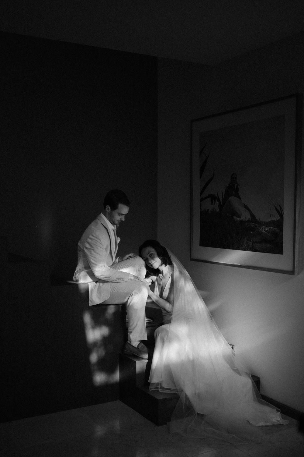 Black and white photo of bride and groom sharing an intimate moment in dramatic light and shadow.