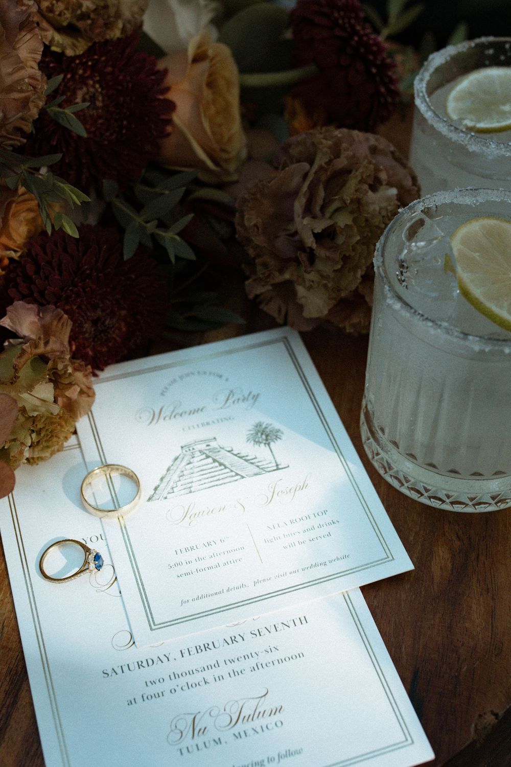 Wedding stationery, gold rings, and margarita glasses styled with burgundy florals in Tulum Mexico.