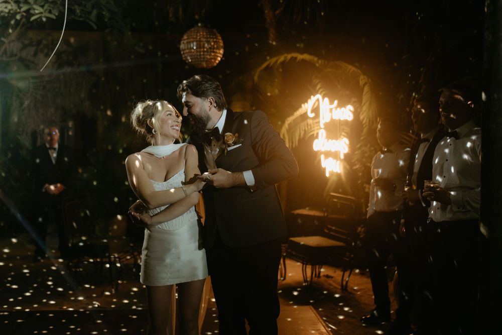 Bride and groom sharing first dance surrounded by confetti and warm glowing lights at night.