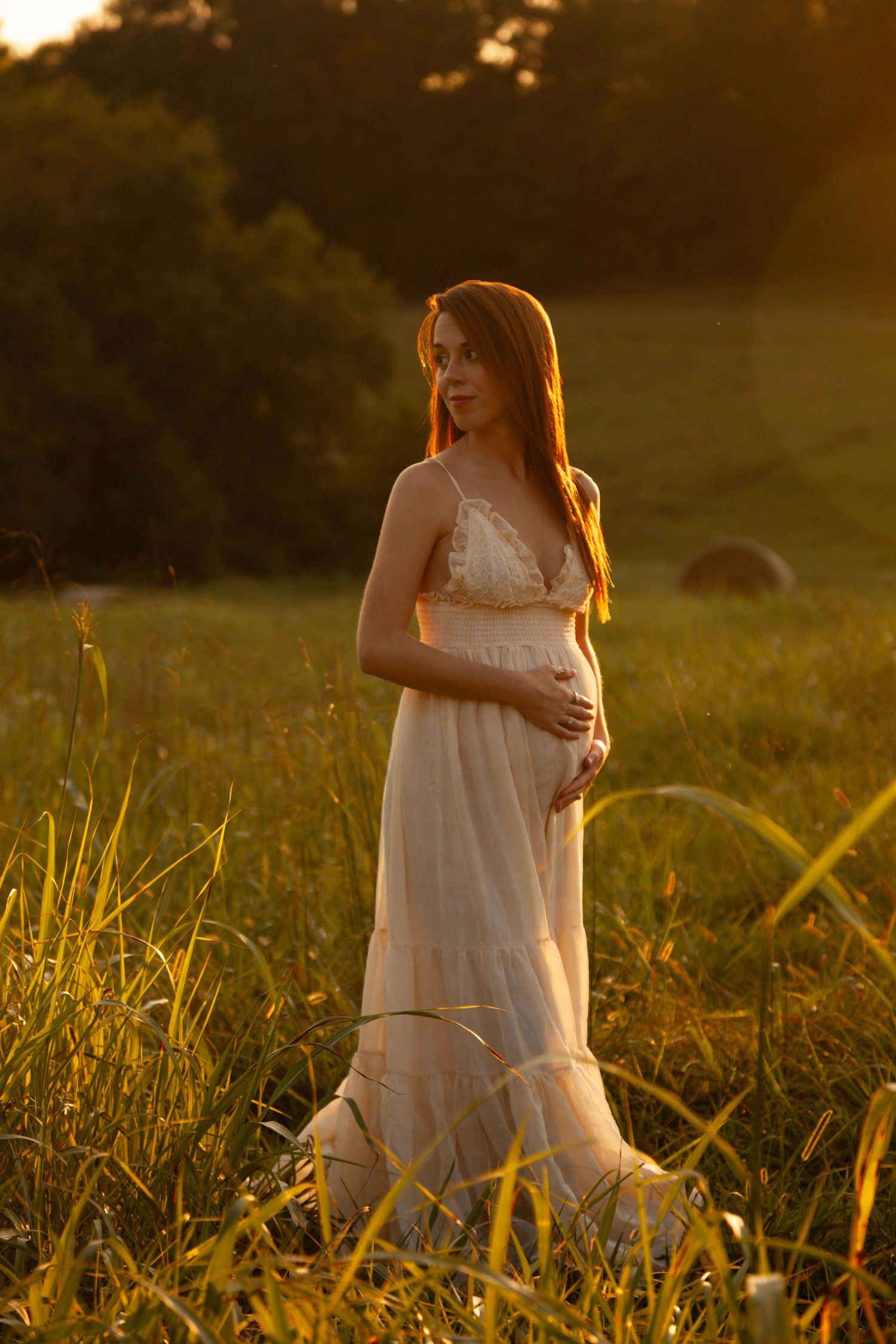 Dreamy maternity portrait in flowing white dress at sunset in a meadow.