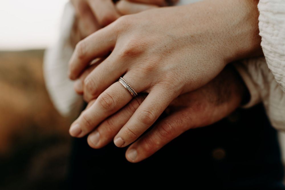 Close-up shot of hands with a wedding ring against a soft blurred background.