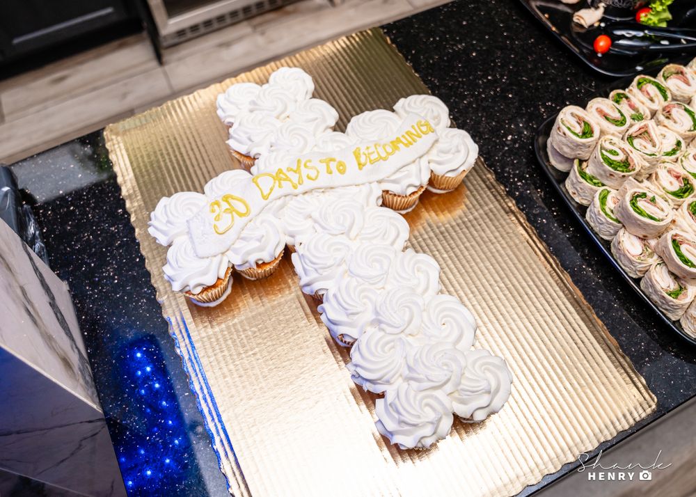 Decorative white cross-shaped cupcake arrangement displayed on dark counter.