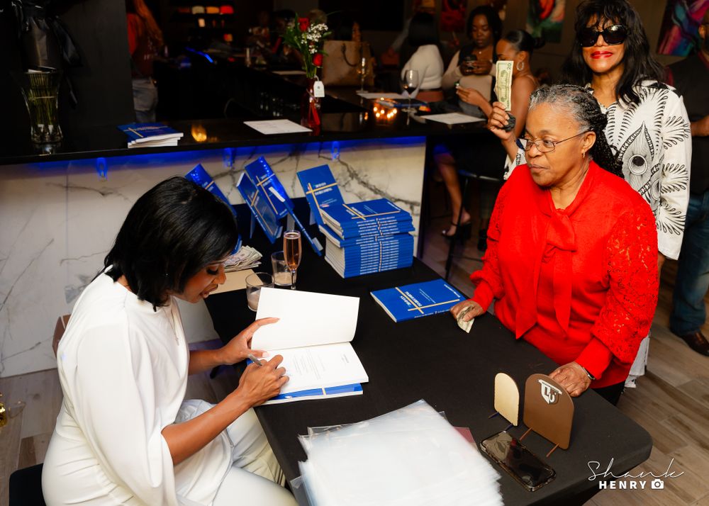Book signing session with people at table exchanging blue books.