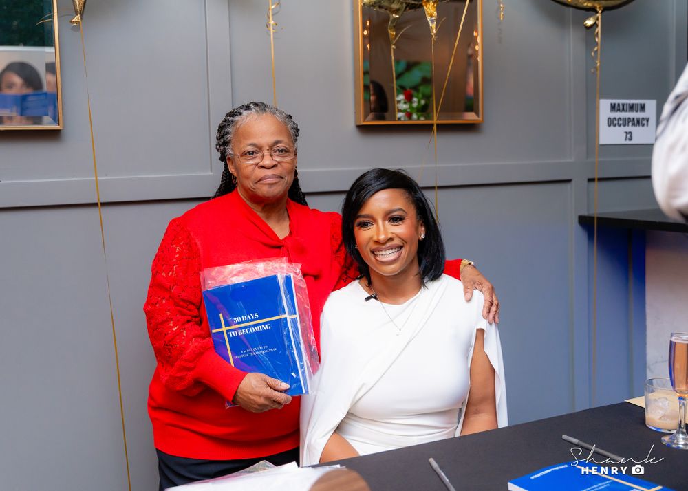 Two people posing with blue book at indoor event.