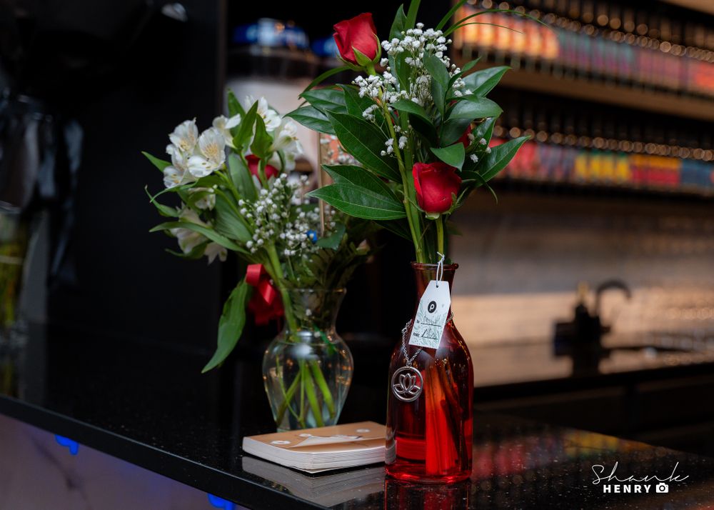 Floral arrangement with red roses in vase next to bottle on dark counter.