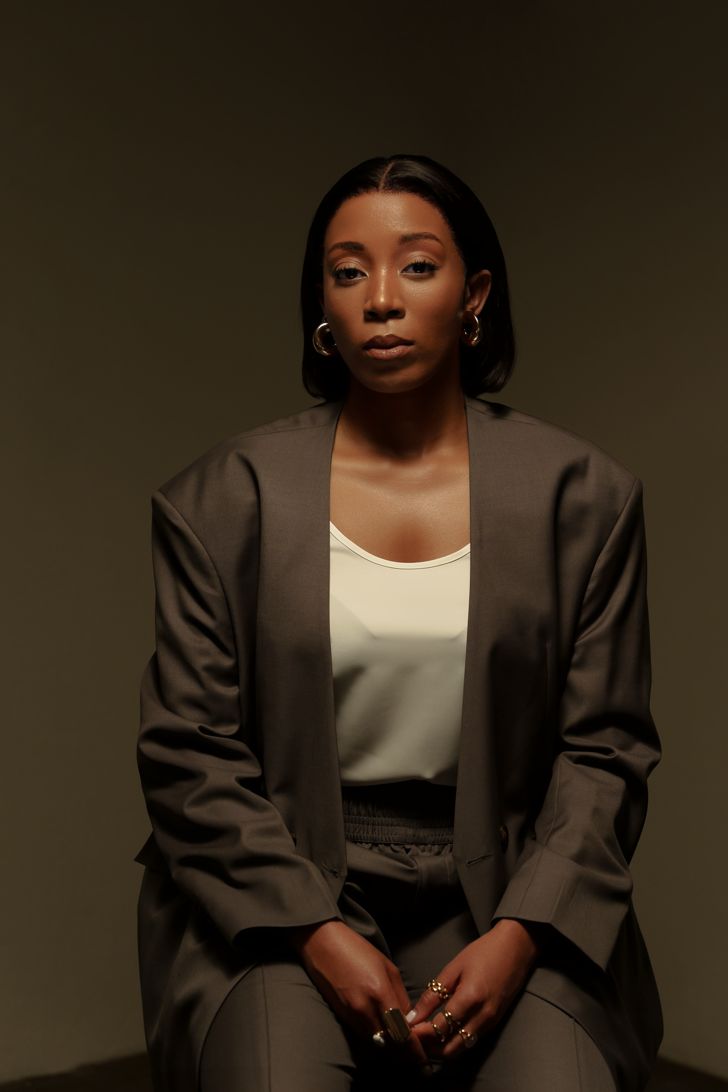 Professional studio portrait of woman in brown blazer and white top against dark background.