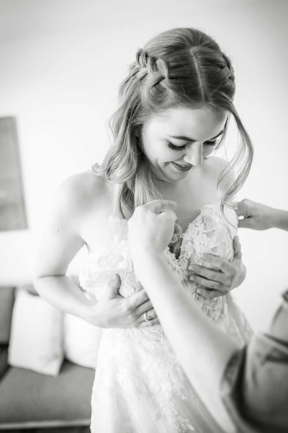 Black and white photo of a bride in lace wedding dress being helped to dress.