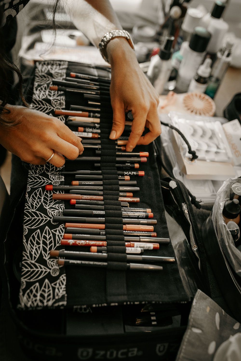 Makeup artist organizing a professional roll-up brush kit filled with cosmetic pencils and brushes on a ZUCA case.