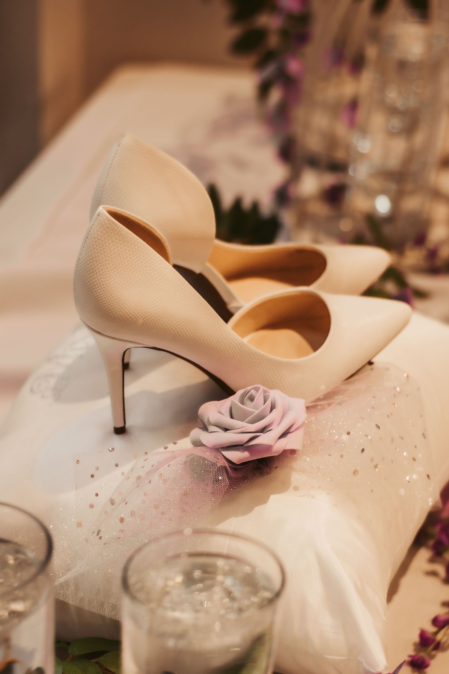 Elegant cream-colored wedding heels with a delicate pink rose decoration on white fabric.