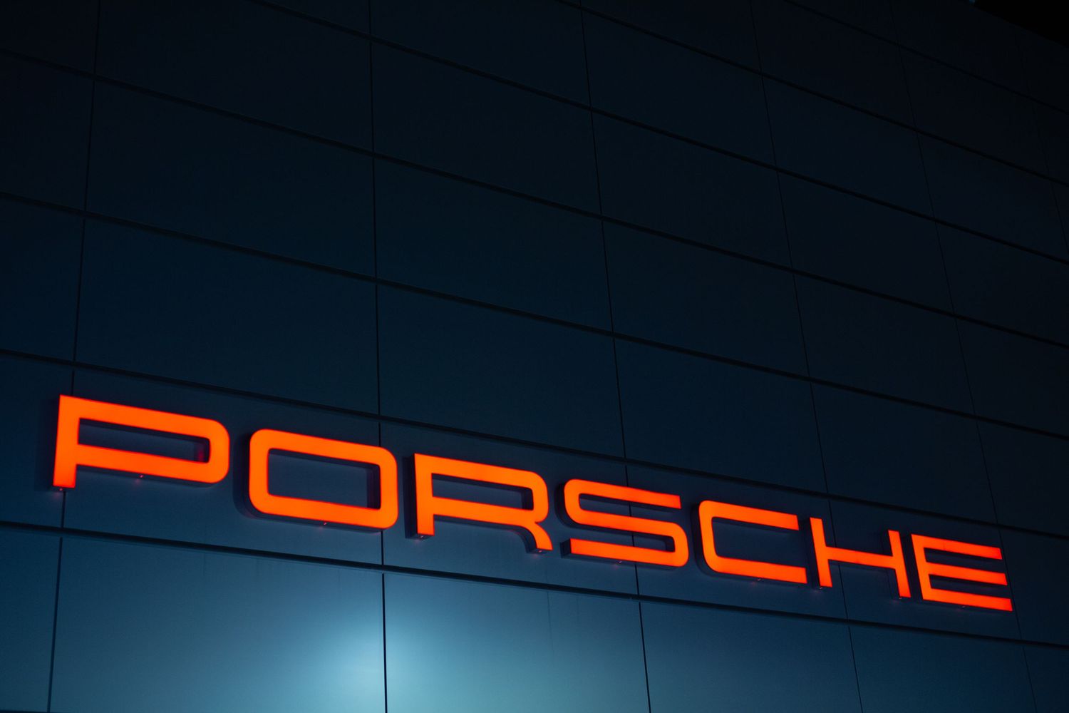 Illuminated Porsche logo signage against dark blue background at night.