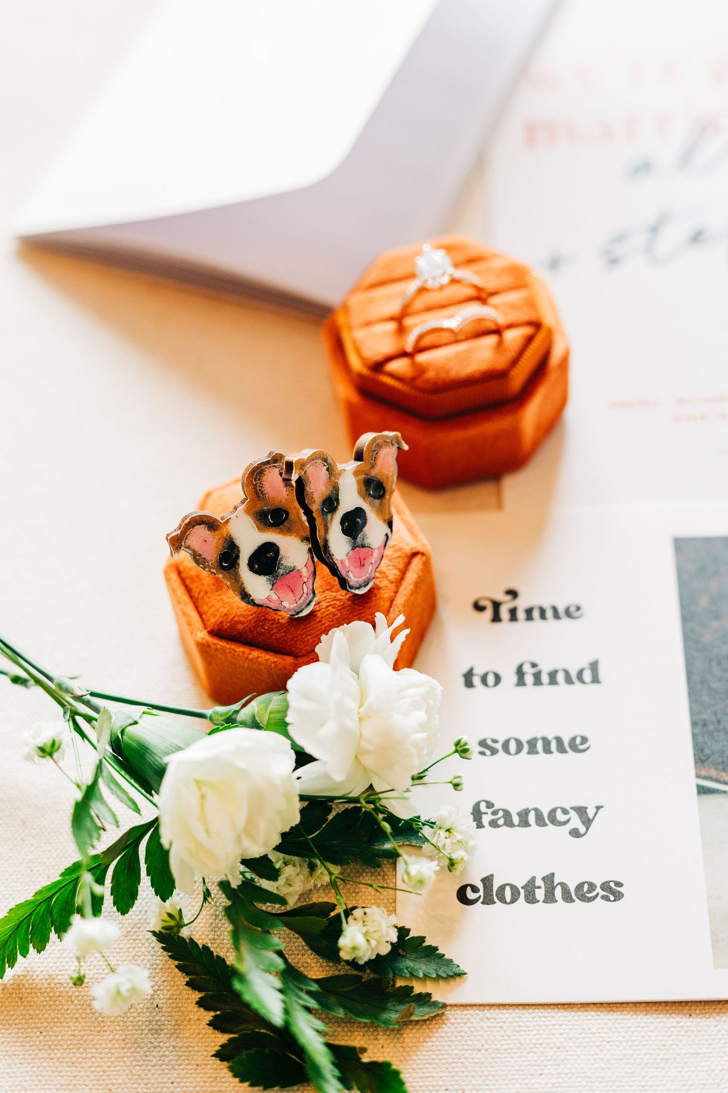 A ring box with a dog design sits next to white flowers and text that says 'time to find some fancy clothes'.