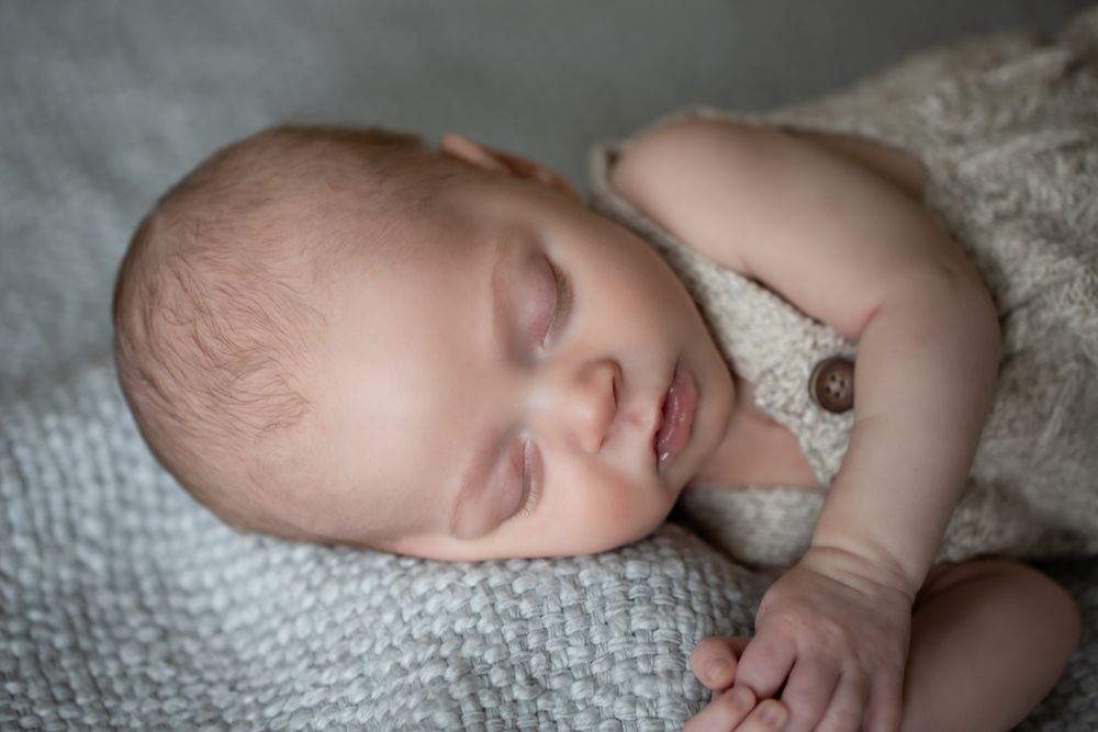 Peaceful newborn baby sleeping on a soft gray knit blanket, wearing a cozy beige outfit, close-up portrait photography.