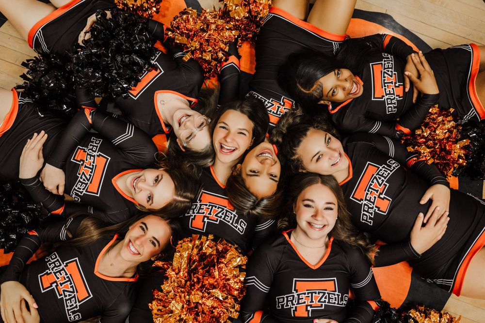 Cheerleaders in black uniforms with orange accents lying in circle formation.