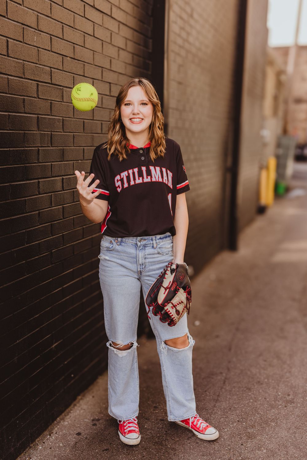 Casual outfit featuring ripped jeans, a black t-shirt, and a yellow softball against a brick wall backdrop.