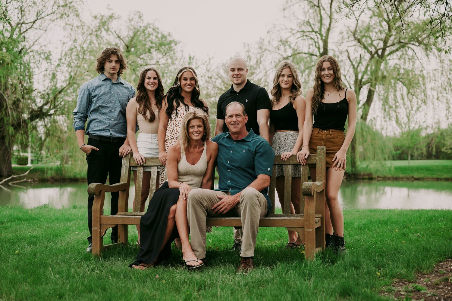 Happy family of seven posing together on wooden benches in a lush green park.