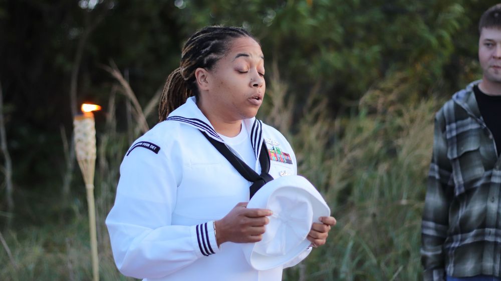 Candid military photography capturing a female U.S. Navy Sailor in Dress Whites holding her cover during a moment of reflection outdoors