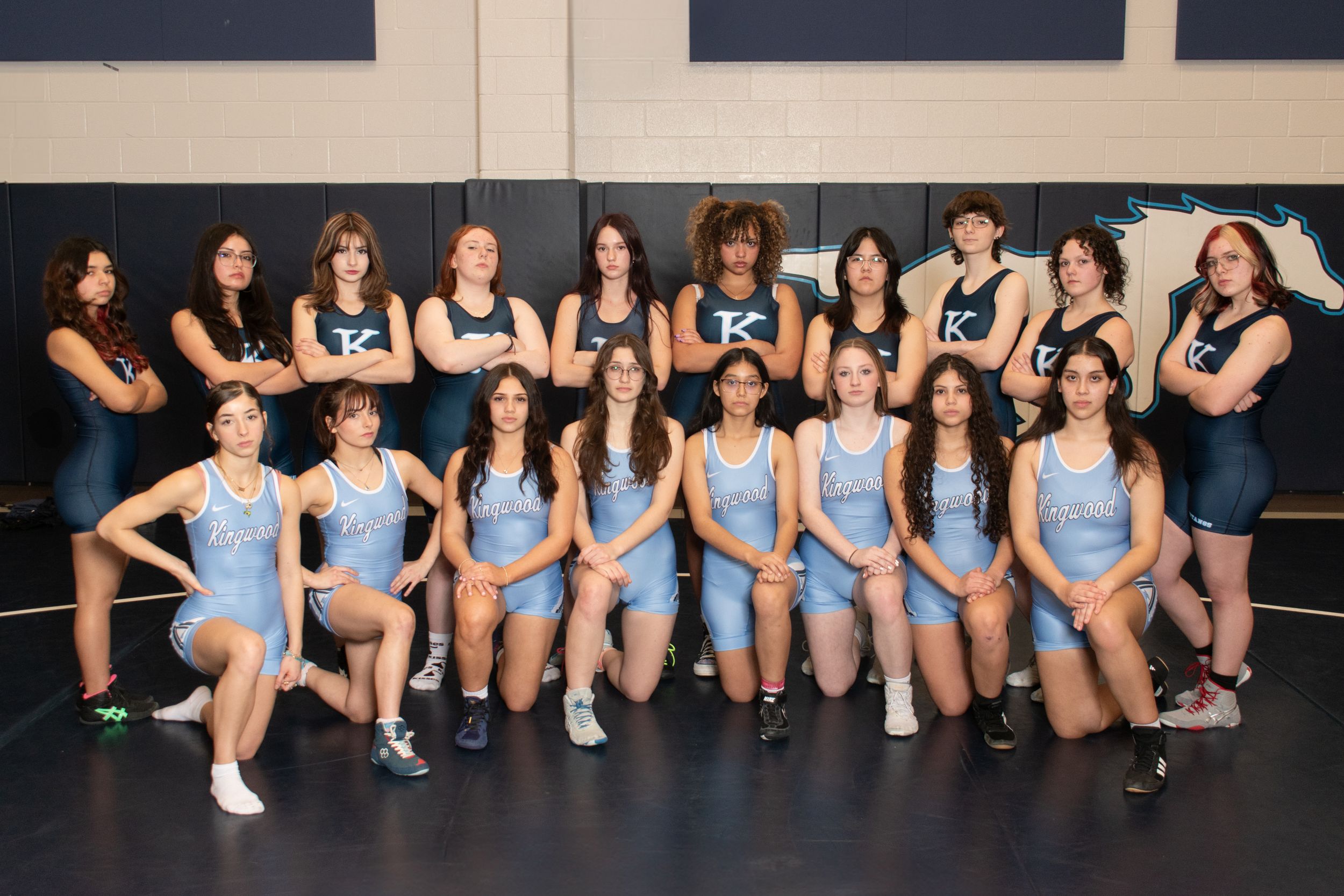 Women's sports team members pose together in light blue uniforms on indoor court.