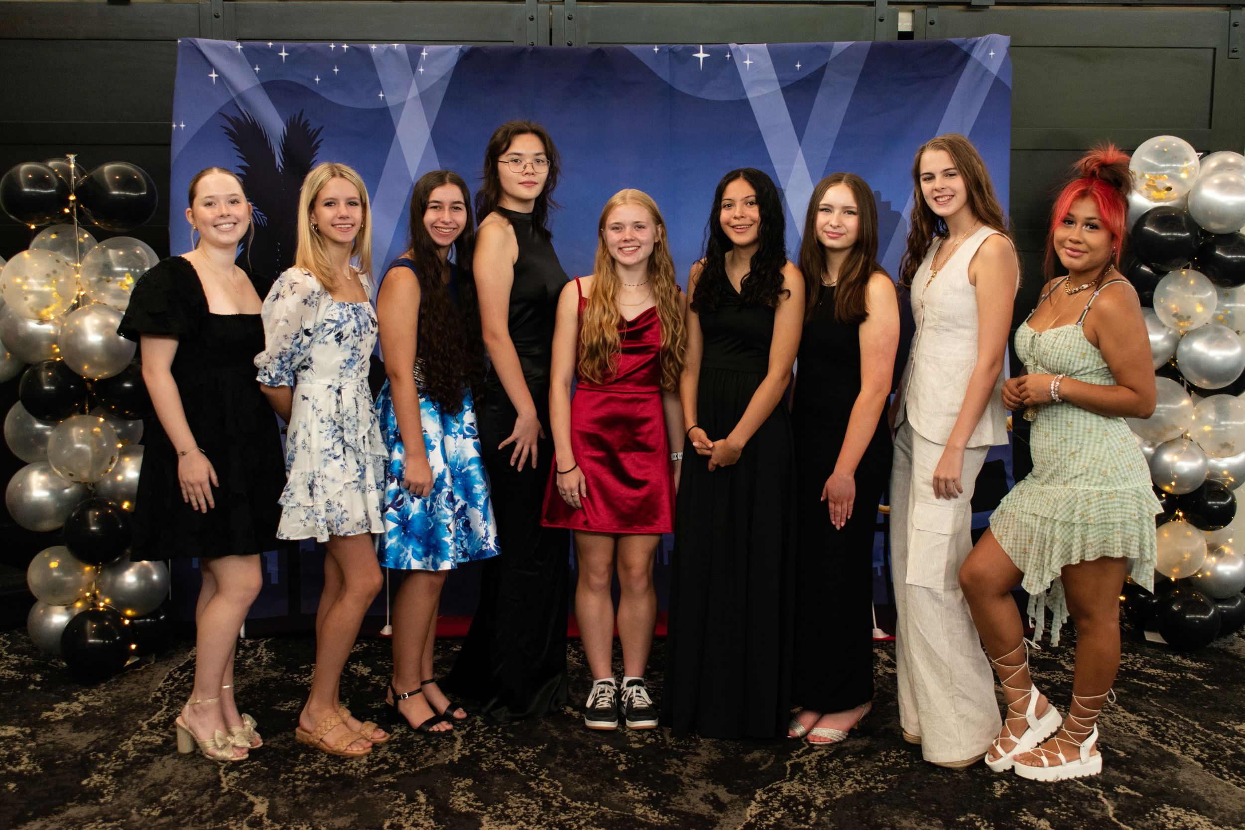 Group photo of people in formal attire standing against a backdrop with silver balloons.