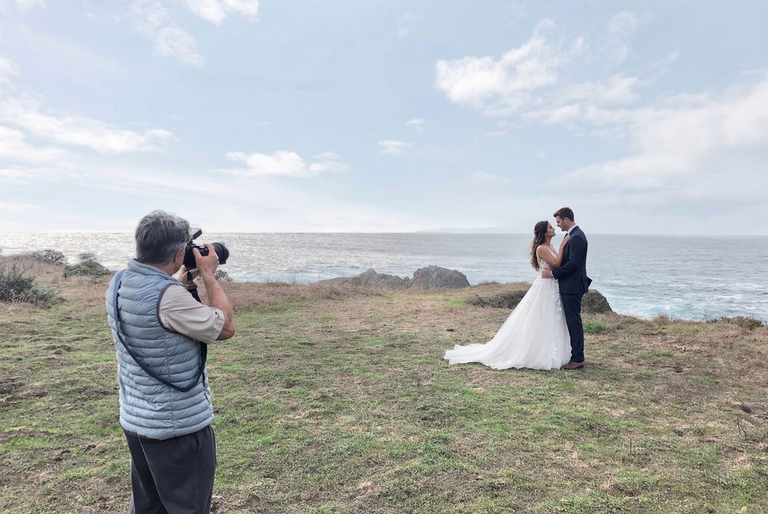 Photographers capturing content near a tall wooden fence structure by the ocean.