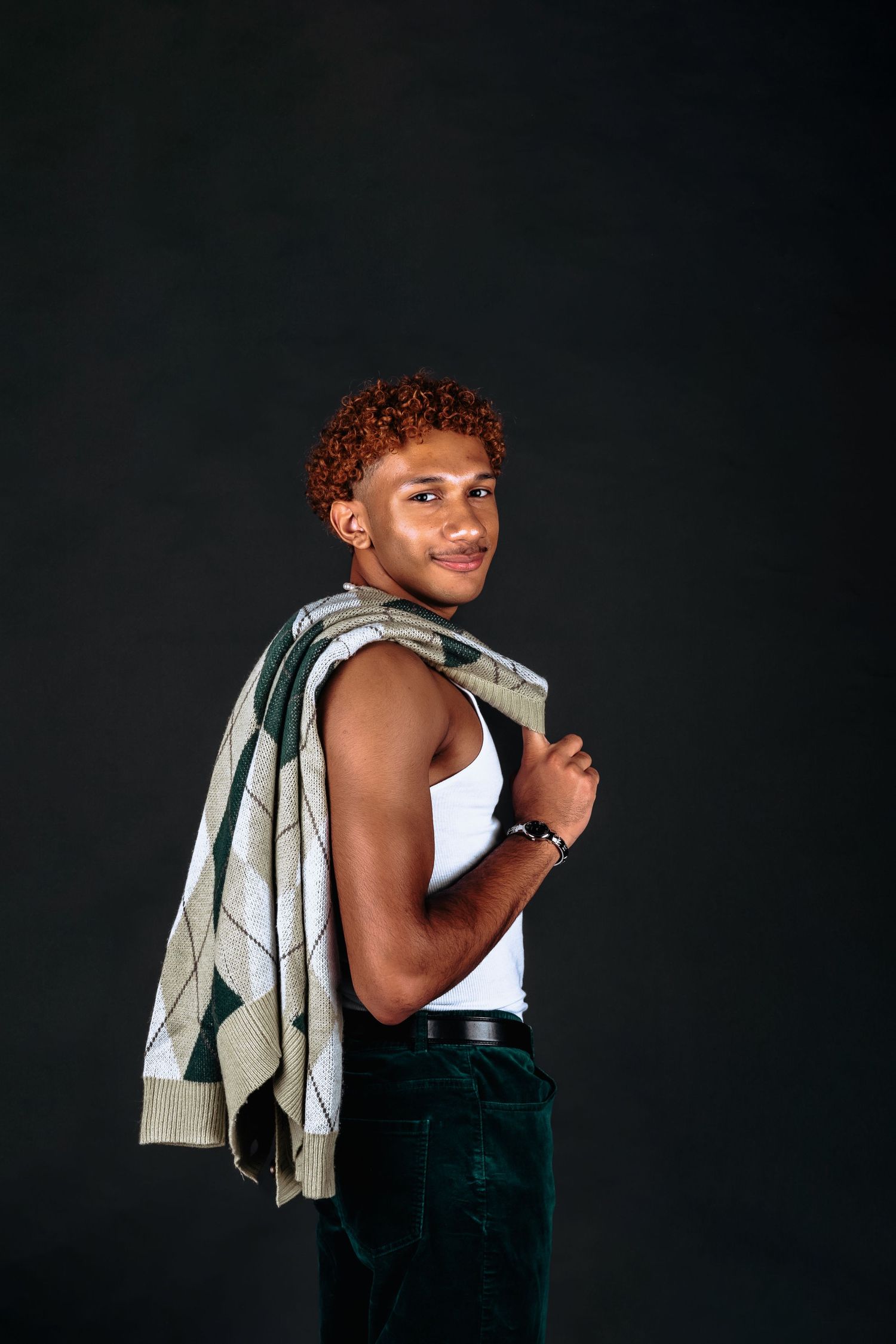 Person wearing dark pants poses playfully against a black background with a cloth over their shoulder.