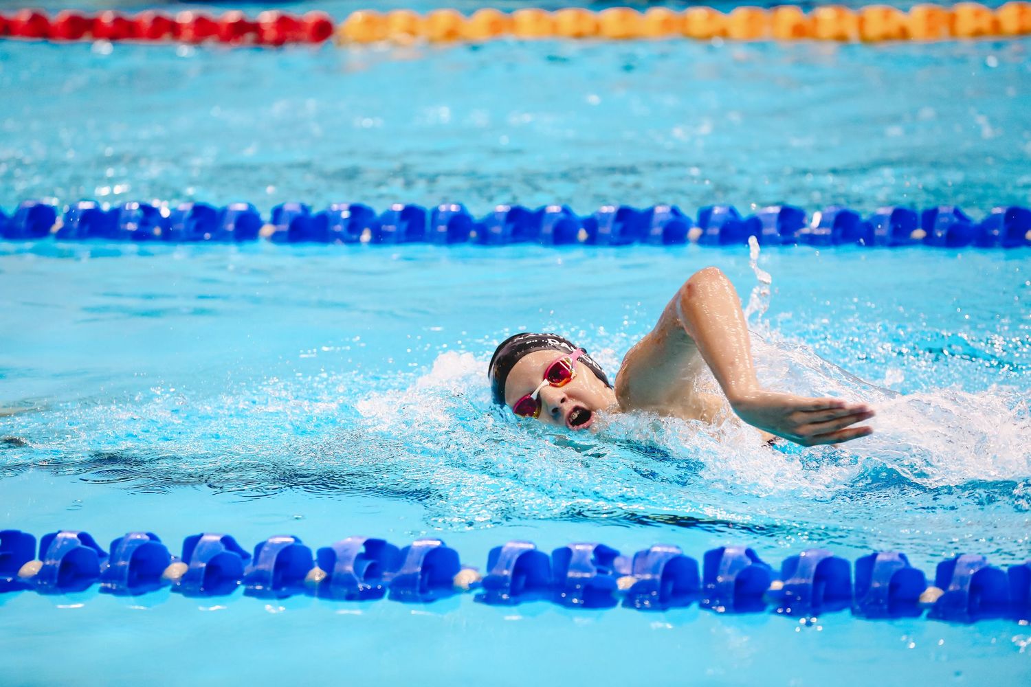Swimmer performing freestyle stroke in pool lane with orange and red lane markers.