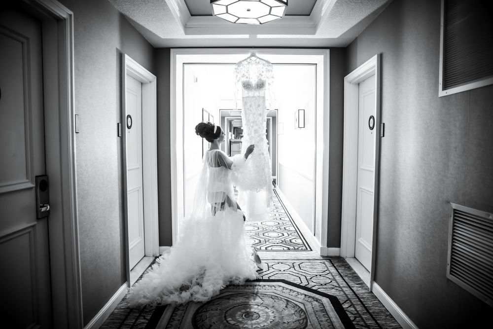 A bride in a flowing white gown walks down an elegant hotel hallway in black and white photography.