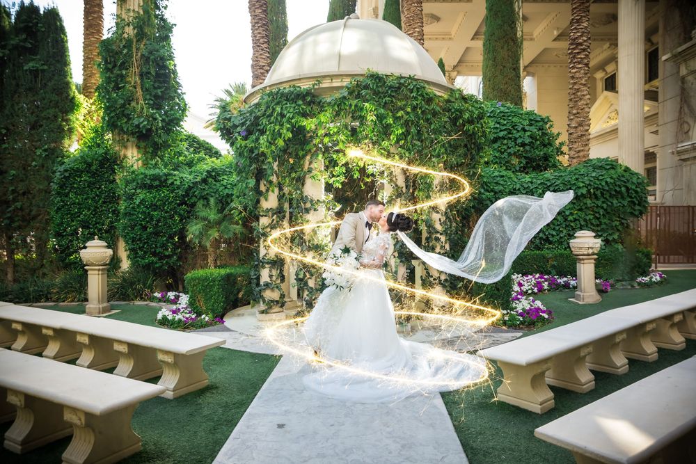 Long white veil flows gracefully in a lush garden courtyard with elegant stone benches and Mediterranean architecture.