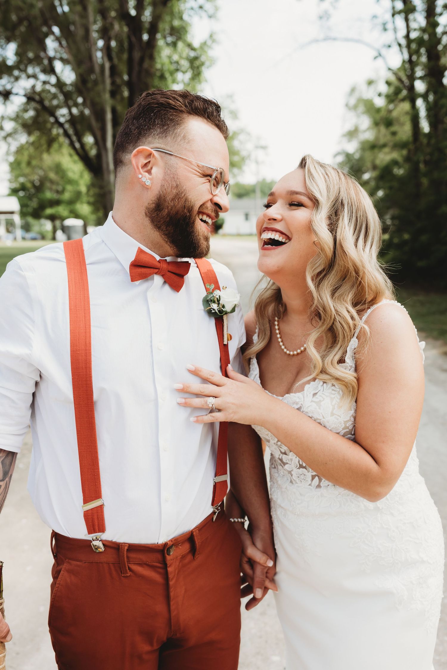 Wedding couple in white and red attire sharing joyful laughter outdoors.