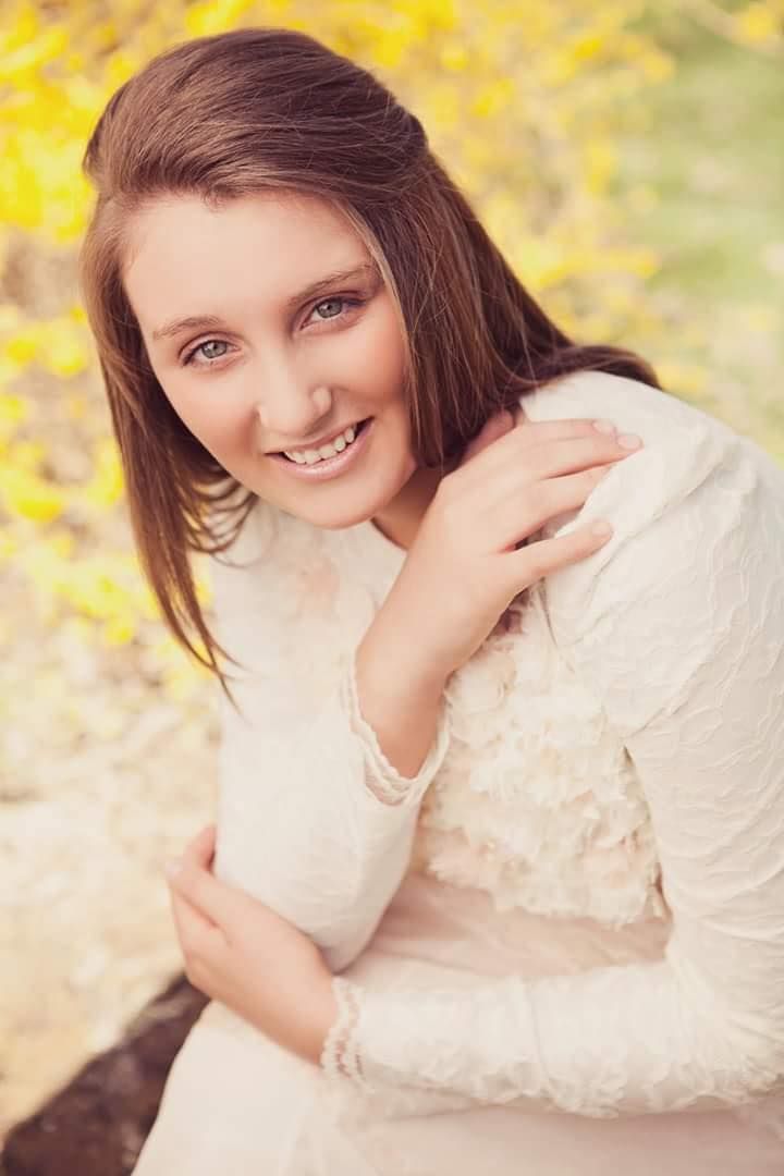 Smiling brunette woman in white lace dress with yellow foliage background.