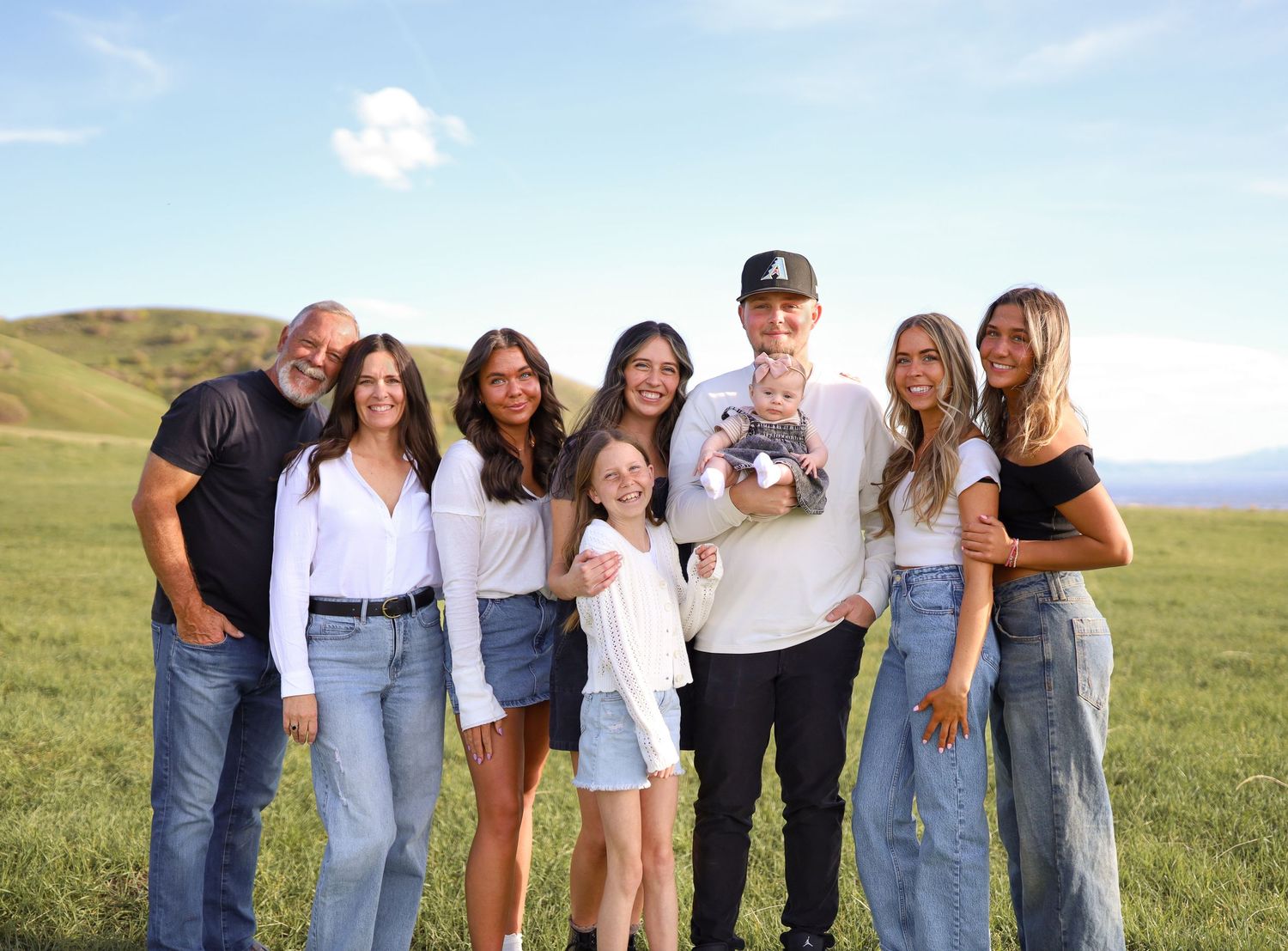 Happy family of seven poses together in a green meadow with rolling hills at sunset.