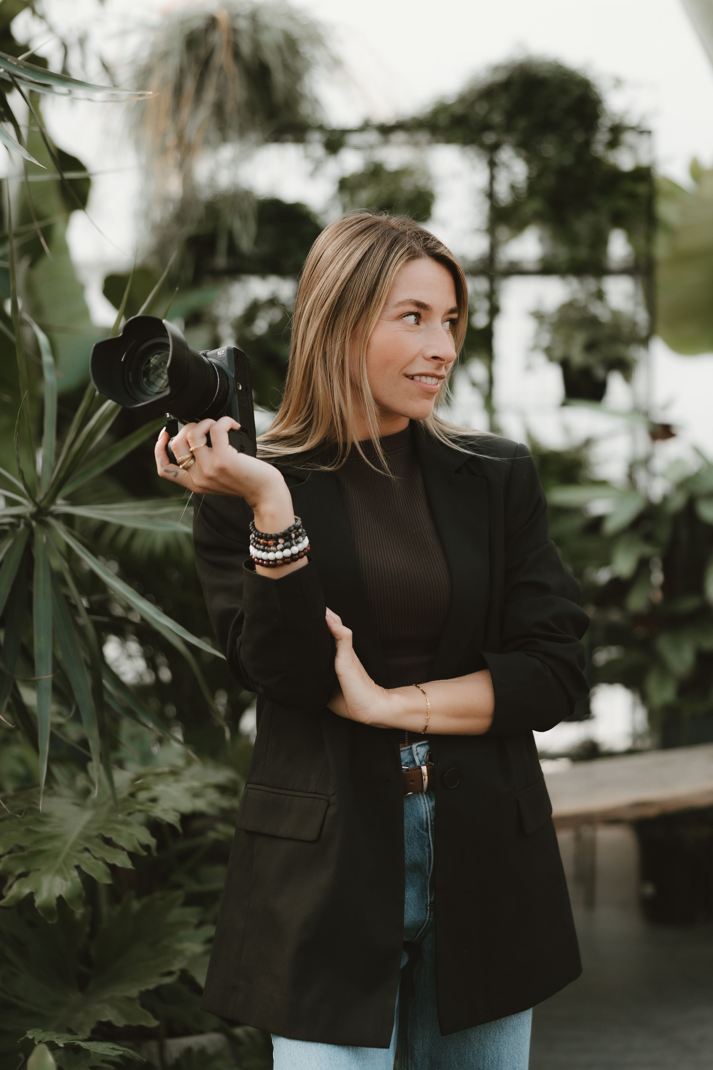 Woman in casual attire poses with a camera while standing on a floral couch.