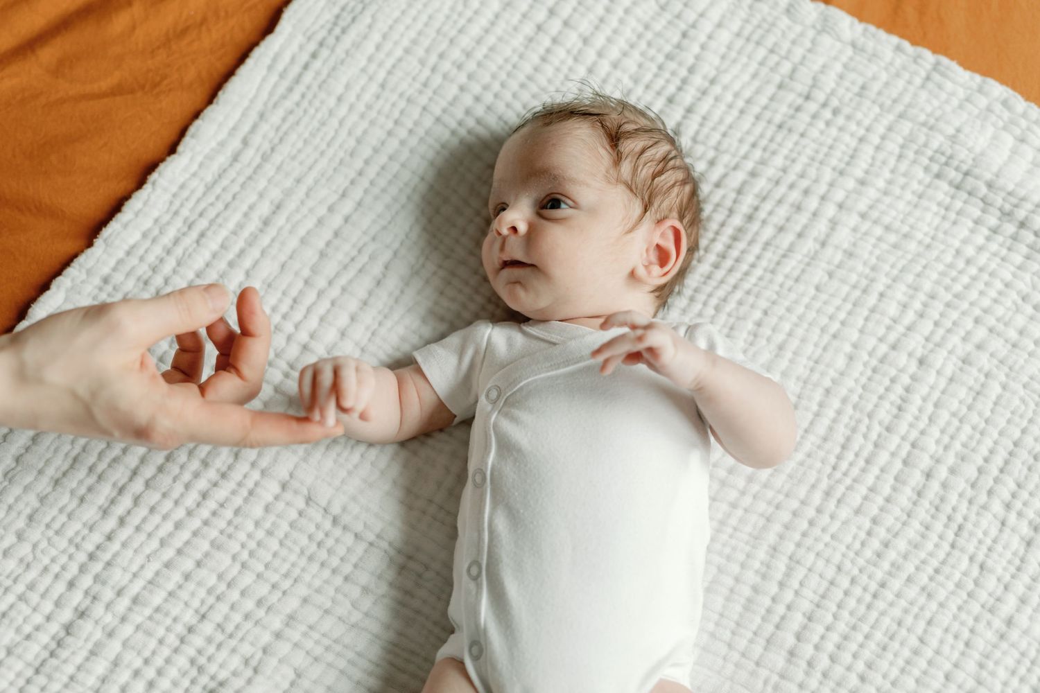 Newborn baby lying on white textured bedding during an intimate photo session.