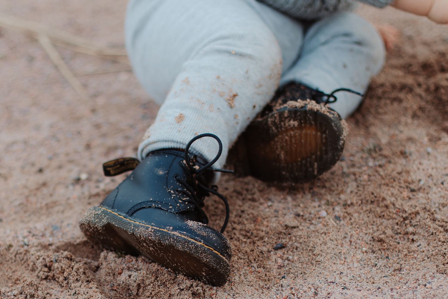 Muddy children's blue boots and denim jeans shown on dirt ground.