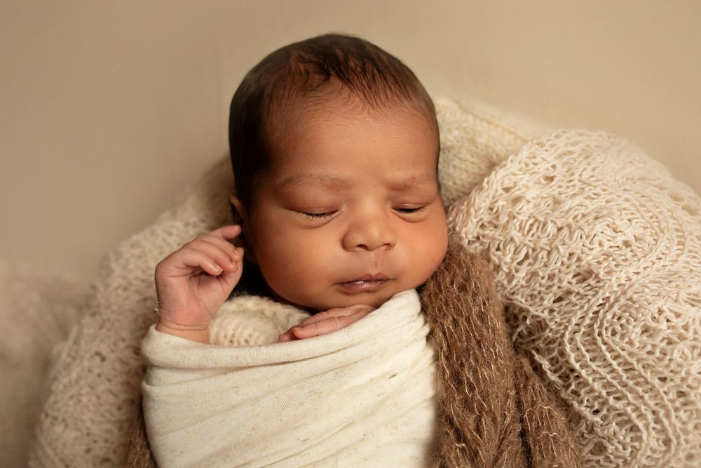 Sleeping newborn wrapped in soft white swaddle against beige background.