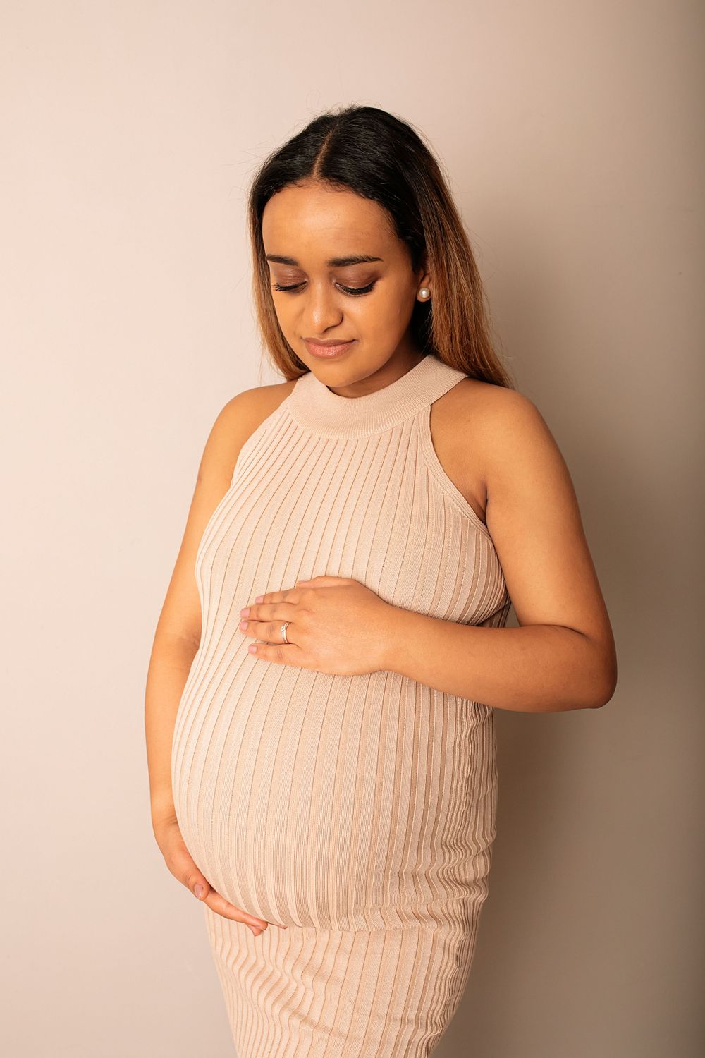 Expectant mother in sleeveless pink dress poses while holding her baby bump.